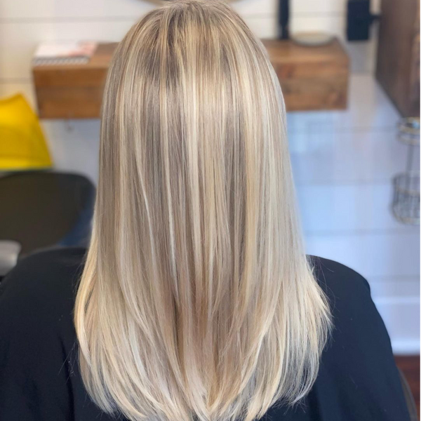 Back view of straight shoulder-length blonde hair with bright highlights and a shadow root, over a black cape