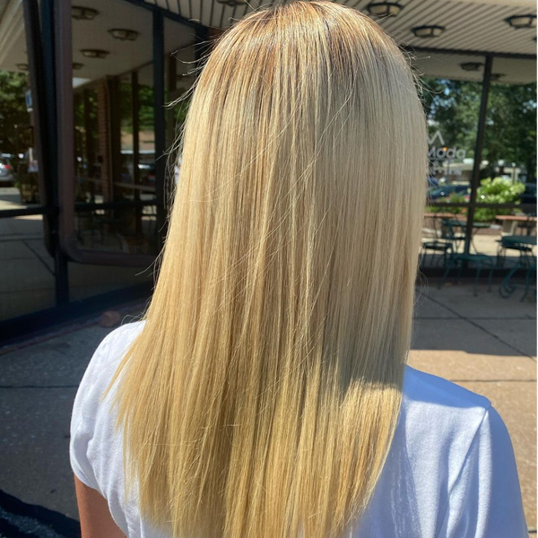 Back view of long straight golden blonde hair with pale ends, worn with a white tee outside a storefront