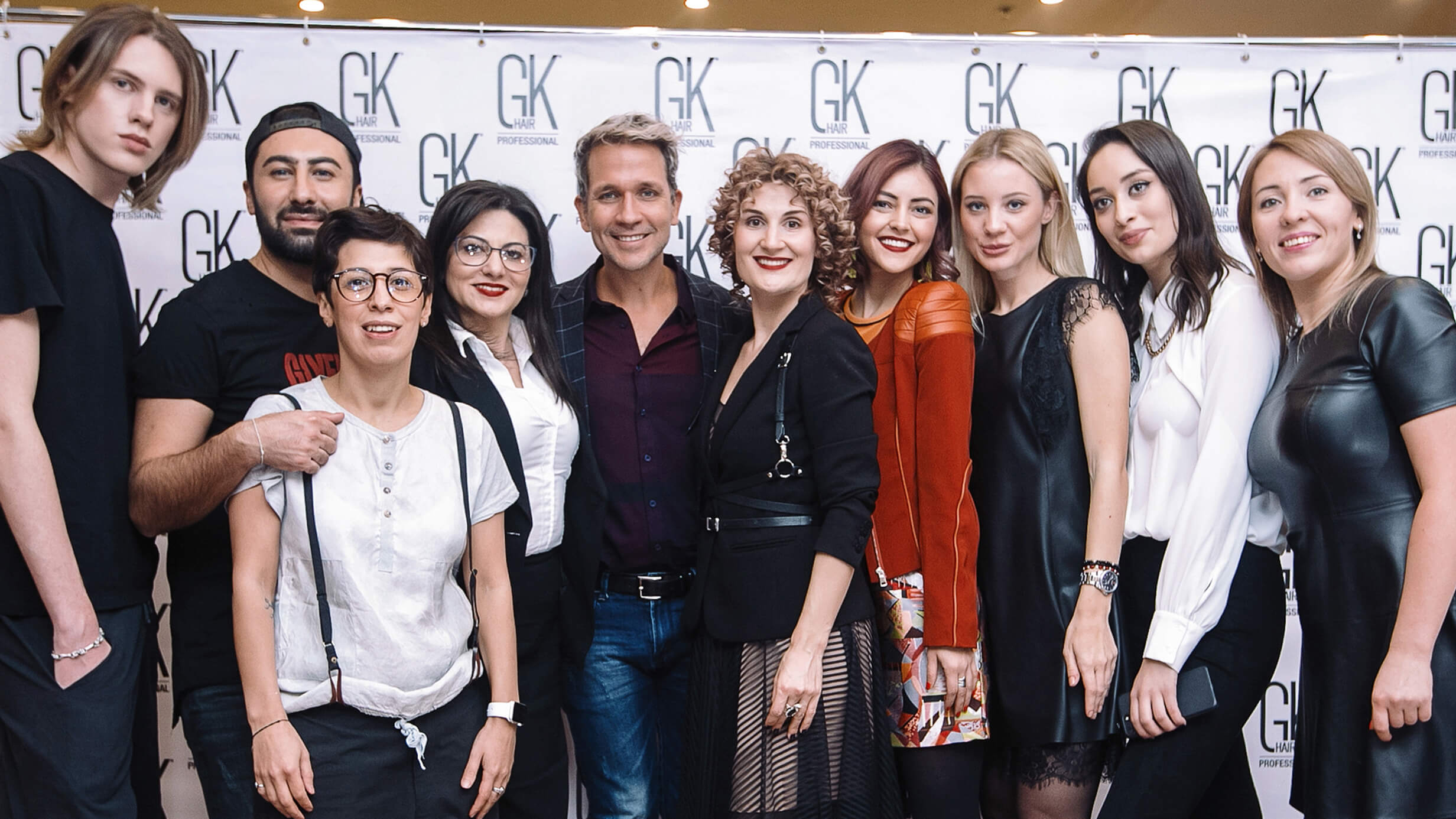 Ten stylists and guests posing together in front of a GK Hair Professional branded backdrop
