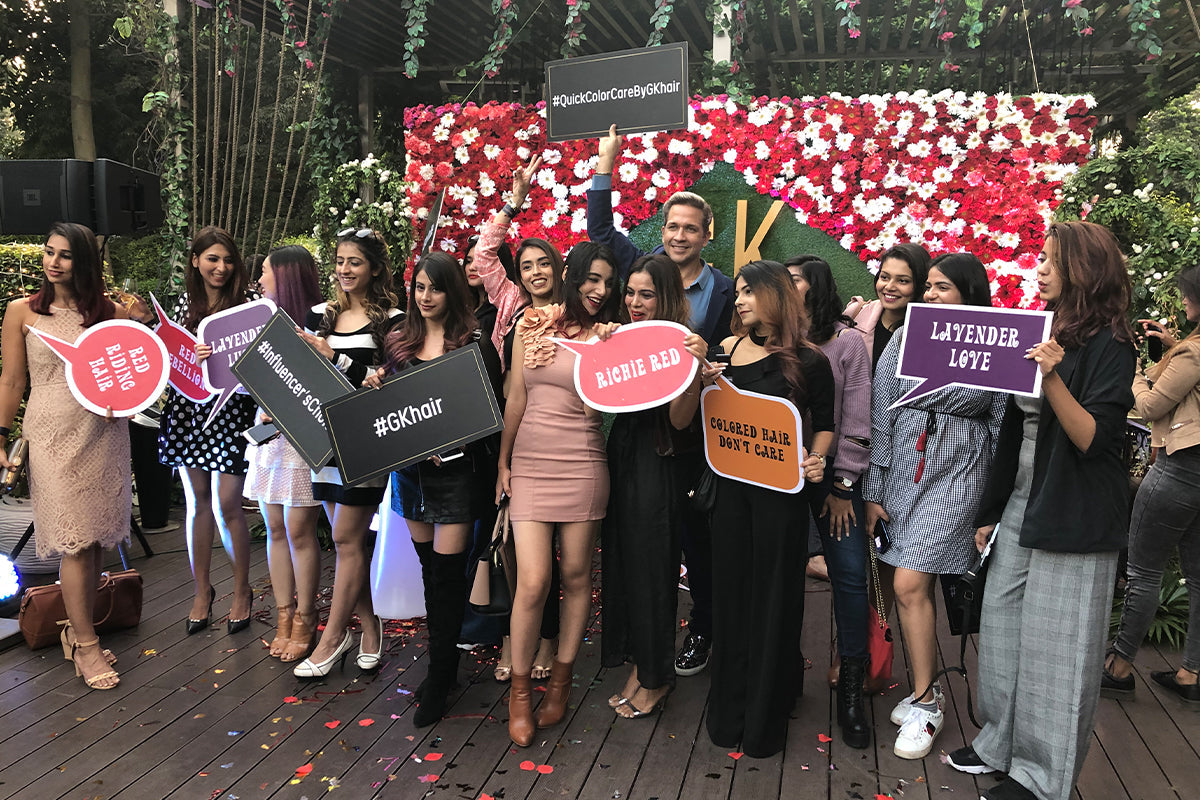 Guests holding speech bubble signs at an outdoor launch event before a red and white floral wall