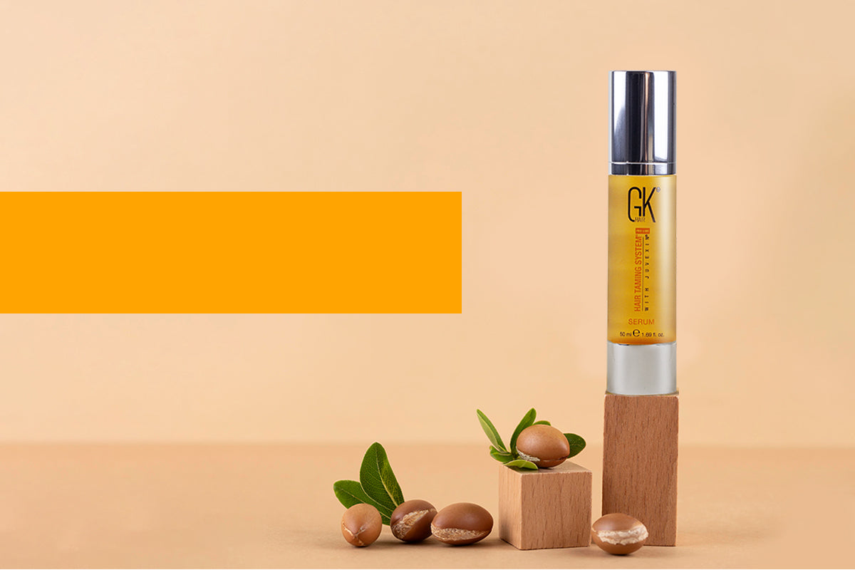 GK Hair serum bottle displayed beside smooth, frizz-free hair strands on a plain background