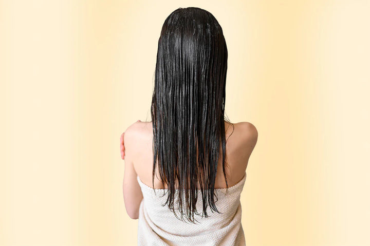 Oily scalp: back view of a woman with long, slick dark hair, wrapped in a white towel