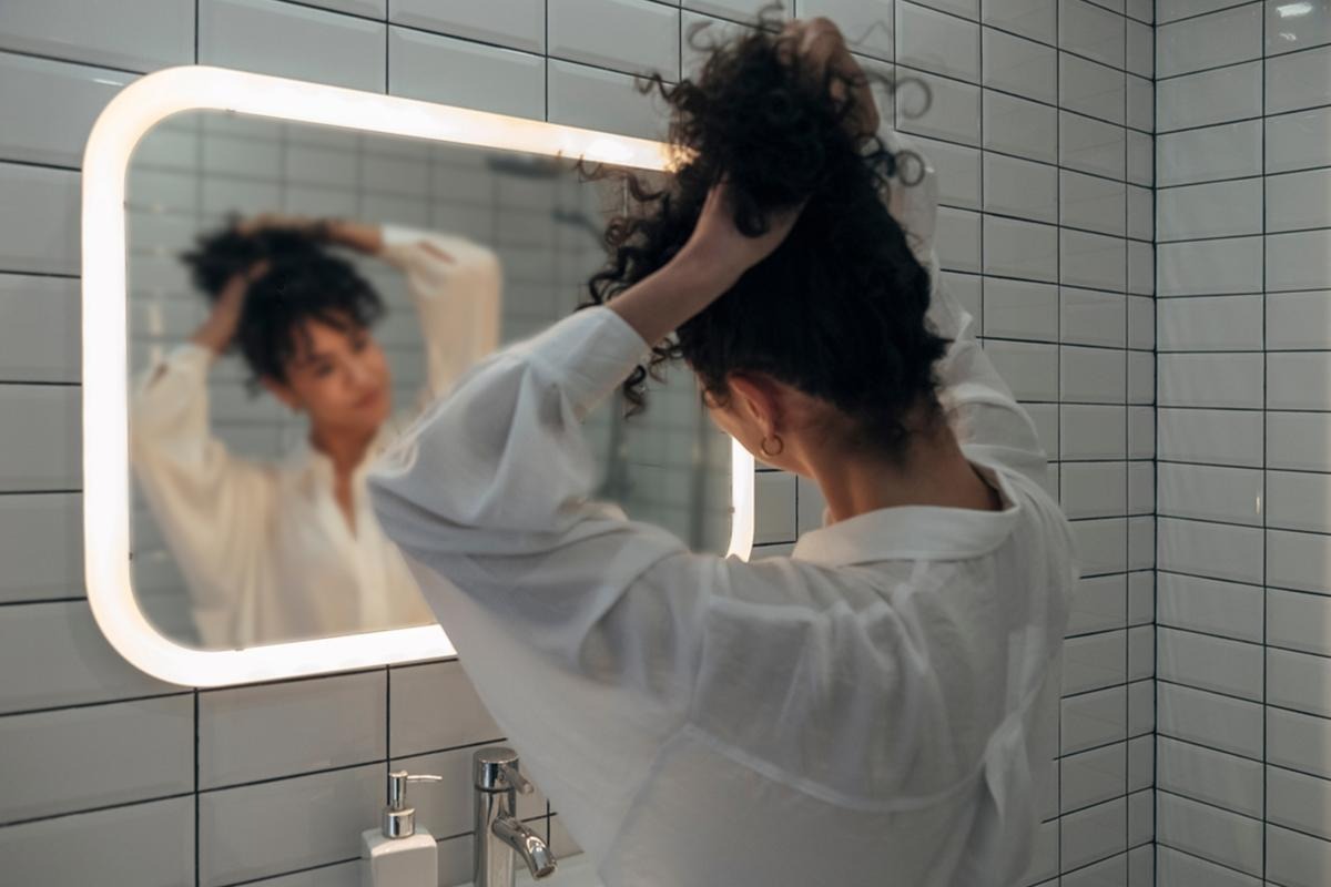 Woman gathering curly hair into a loose pineapple at the top of her head before bed