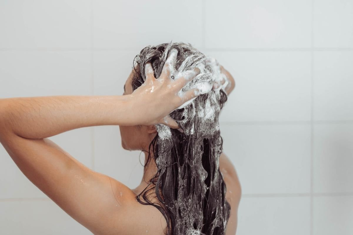 Woman lathering shampoo into wet hair while washing it in the shower