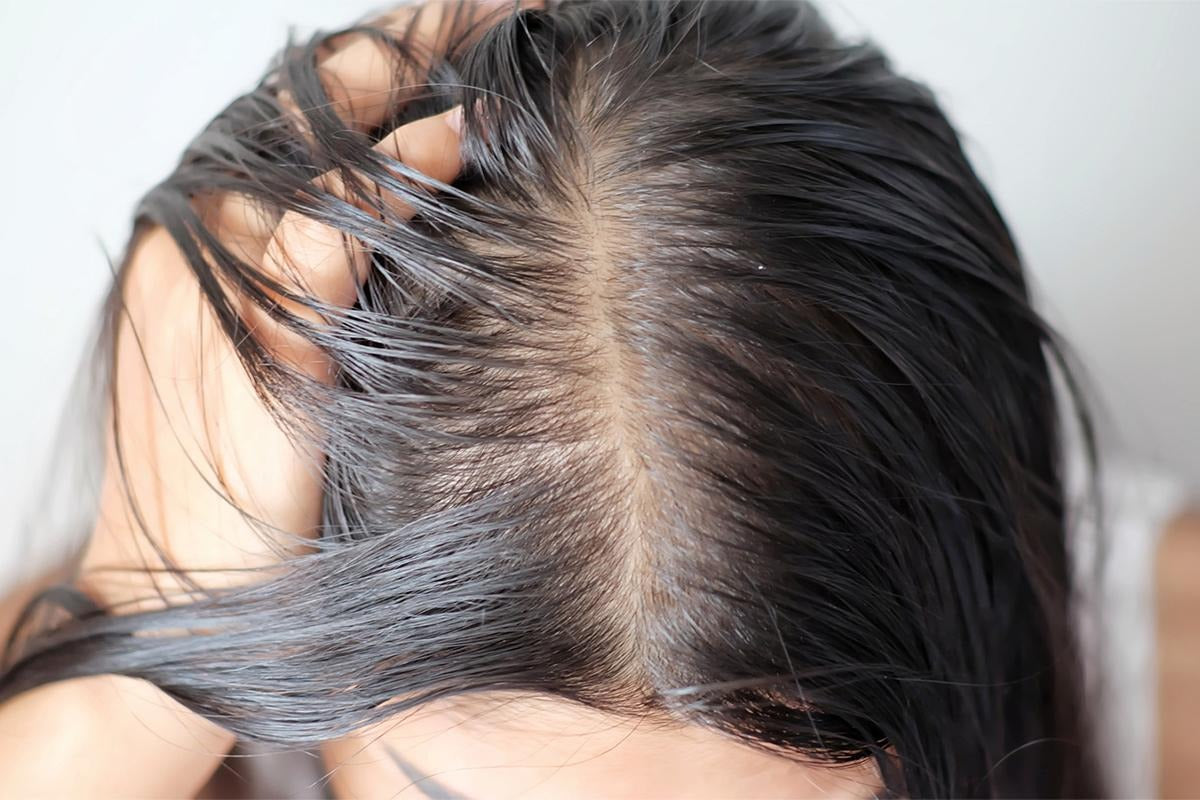 Woman with fine, oily hair checking greasy roots at her scalp in the mirror