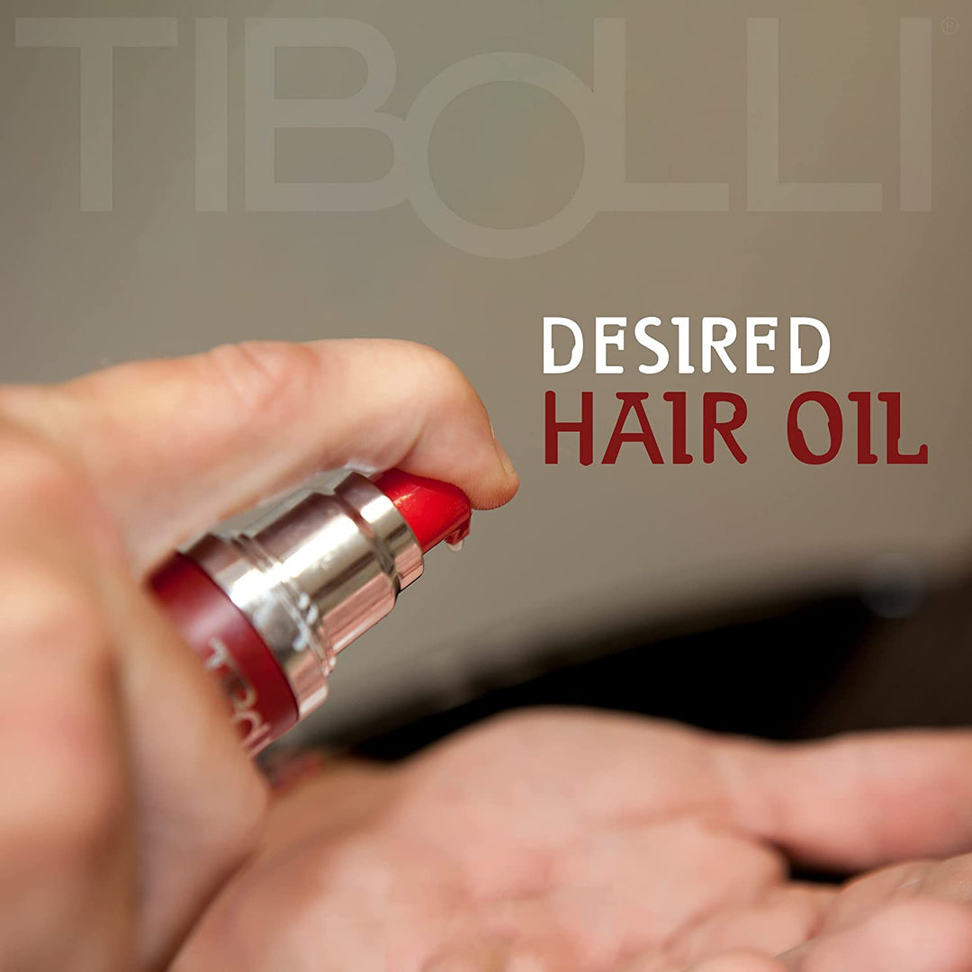 Hand pumping oil from a red Tibolli Desired Hair Oil bottle into a cupped palm, with the words Desired Hair Oil alongside