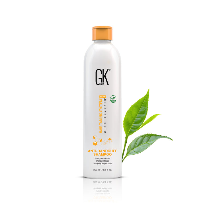 GK Hair Anti-Dandruff Shampoo 250 ml white bottle with an orange cap and vegan badge, beside green tea leaves on white