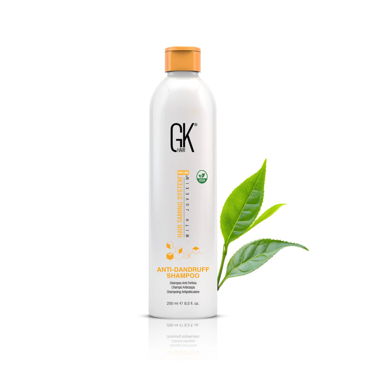GK Hair Anti-Dandruff Shampoo 250 ml / 8.5 fl. oz. bottle with an orange cap, green tea leaves at its side on white