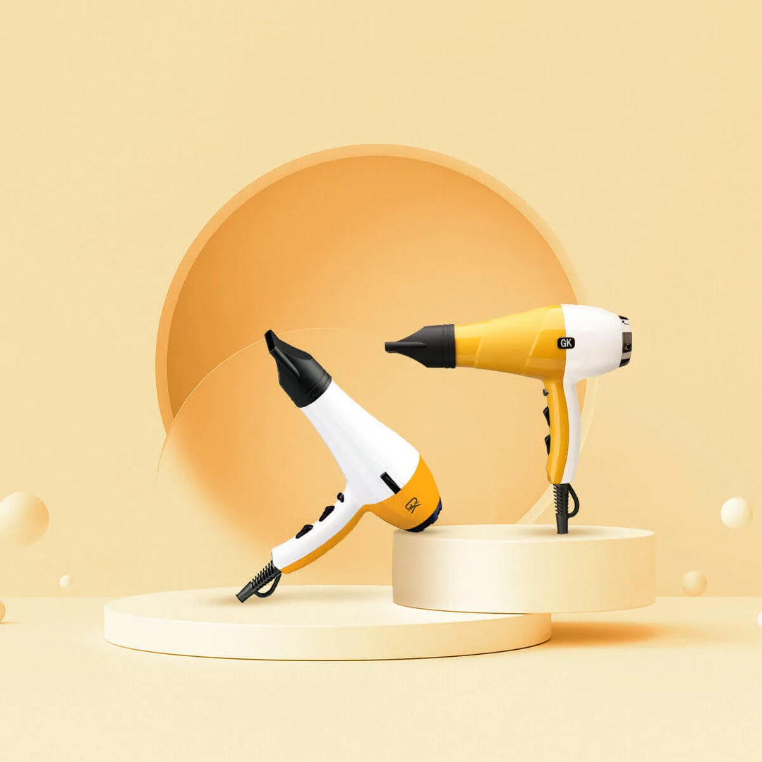 Product shot of two GK Hair dryers in yellow and white on stepped cream plinths with a peach circle behind