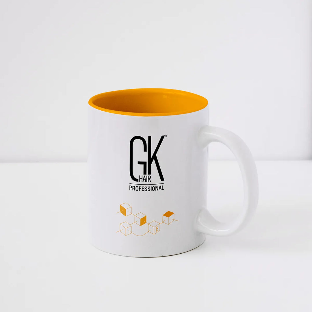 GK Hair coffee mug in white with a bright orange interior, black GK Hair Professional logo and orange Juvexin cube motif