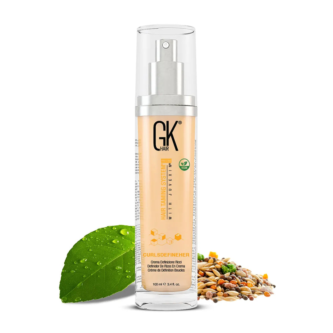 GK Hair CurlsDefineHer 100 ml pump bottle of peach curl cream beside a dewy green leaf and a pile of mixed seeds