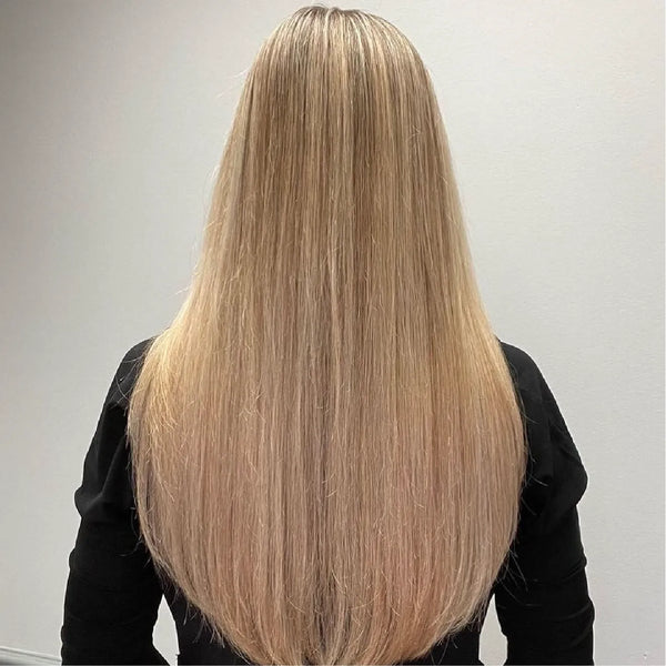 Back view of long, poker-straight golden blonde hair past the shoulders, black top, plain gray wall behind