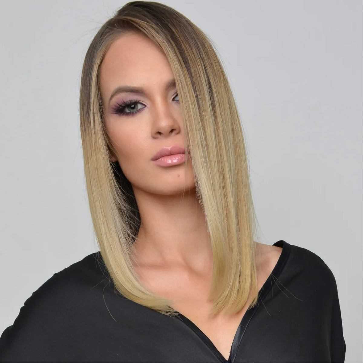 Studio portrait of a model with a sleek shoulder-length blonde lob, dark roots, plum smoky eyes and a black top