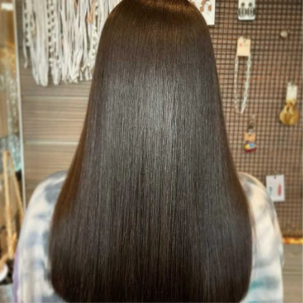 Back view of long, mirror-smooth dark brown hair on a woman in a tie-dye top, salon accessory display behind