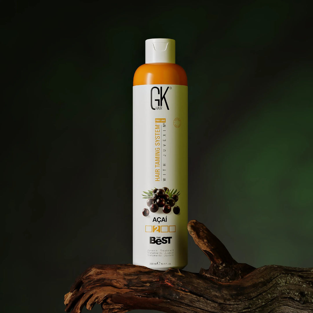 GK Hair The Best Acai Juvexin treatment, 300 ml white bottle with orange shoulder, on driftwood against a dark green backdrop