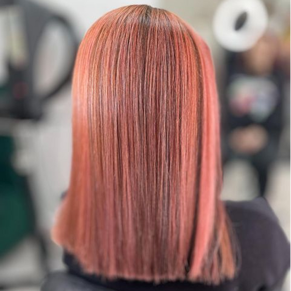 Back view of a sleek straight coral-pink shoulder-length cut with dark roots, shot in a salon