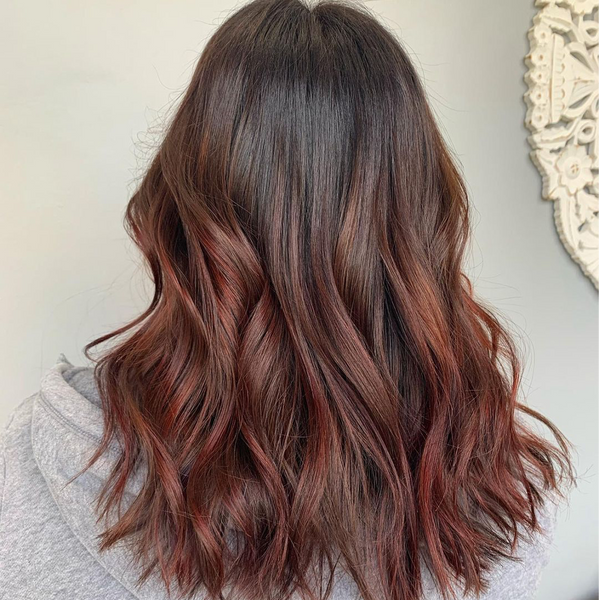 Back view of dark brown hair with copper-red balayage waves falling over a gray hooded sweatshirt
