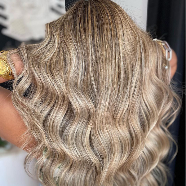Back view of loose beige-blonde waves with icy highlights, hands with a gold watch lifting the ends