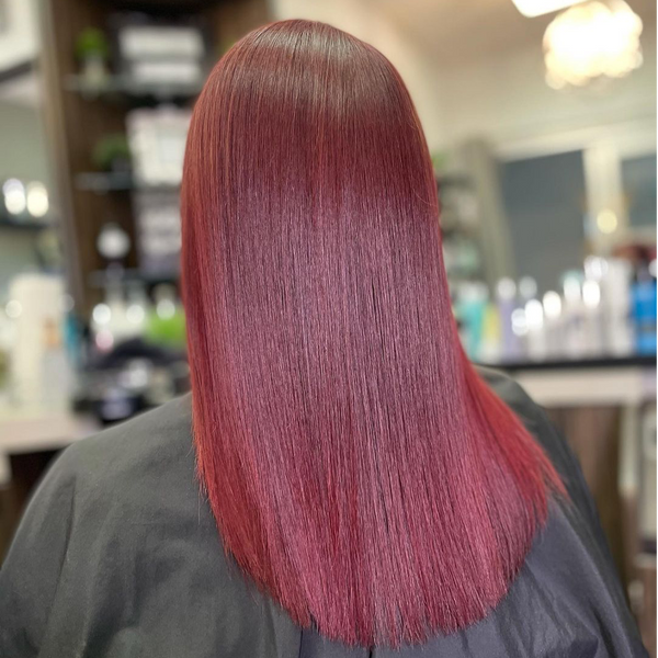 Back view of glossy straight magenta-red hair with a lighter root, over a gray salon cape