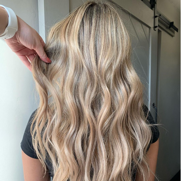 Back view of long sandy blonde beach waves, a hand with a white watch lifting a section at a barn door