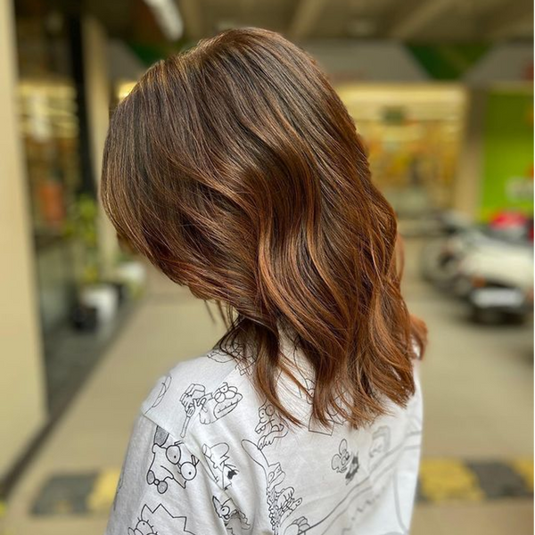 Wavy shoulder-length brown lob with copper and caramel balayage, side view, worn with a cartoon-print white tee in a mall