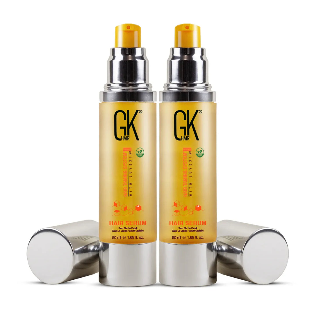 Two 50 ml GK Hair Hair Serum bottles with yellow pumps exposed and their silver caps lying beside them on white