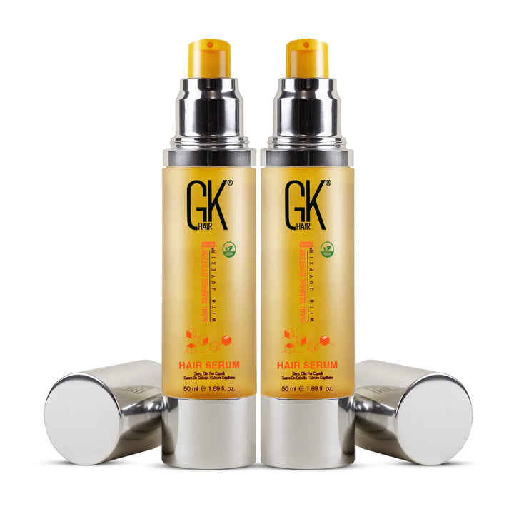 Two 50 ml GK Hair Hair Serum bottles with yellow pumps exposed and their silver caps lying beside them on white