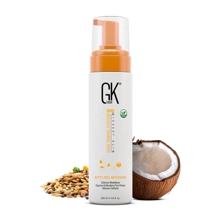 GK Hair Styling Mousse, 250 ml white bottle with orange pump cap, mixed grains at left and a cracked coconut at right