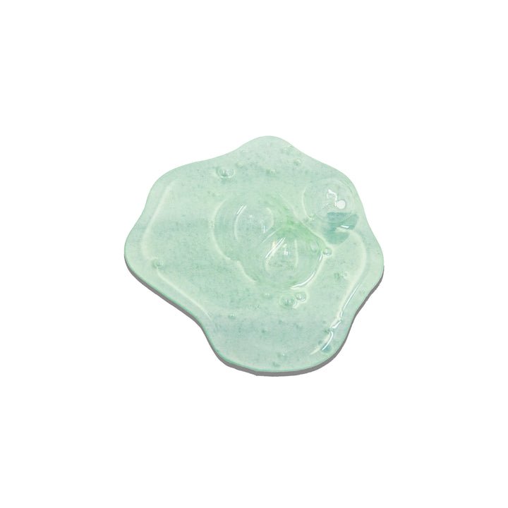 Texture close-up of a glossy swirl of translucent pale green hair gel dotted with air bubbles on a white background