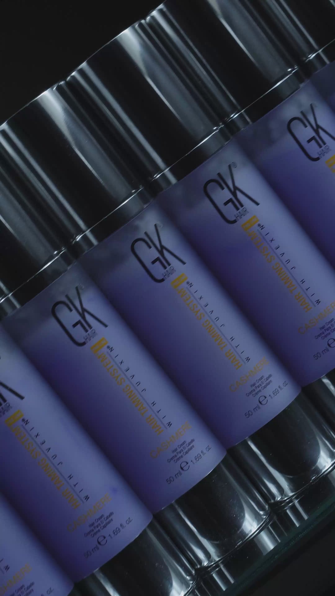 Rows of GK Hair Cashmere hair cream 50 ml lavender bottles with chrome pumps, then one standing alone against black