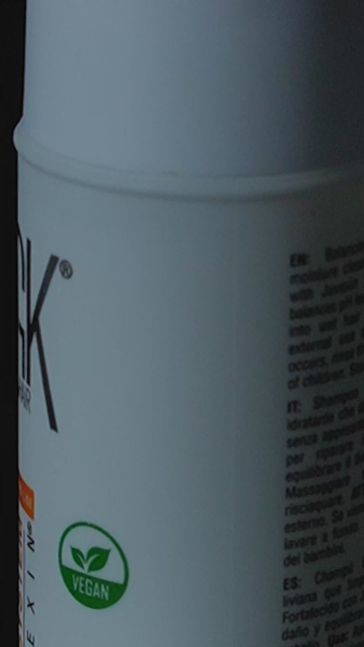 GK Hair Balancing Shampoo bottle tilted against black with a pearly drop running from its cap, vegan badge on the label