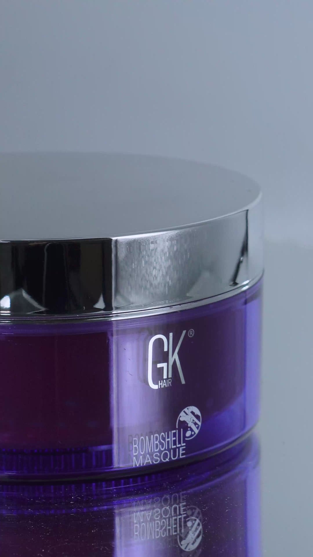 GK Hair Bombshell Masque purple jar with chrome lid, opened to show a deep red masque swirled and lifted on a spatula
