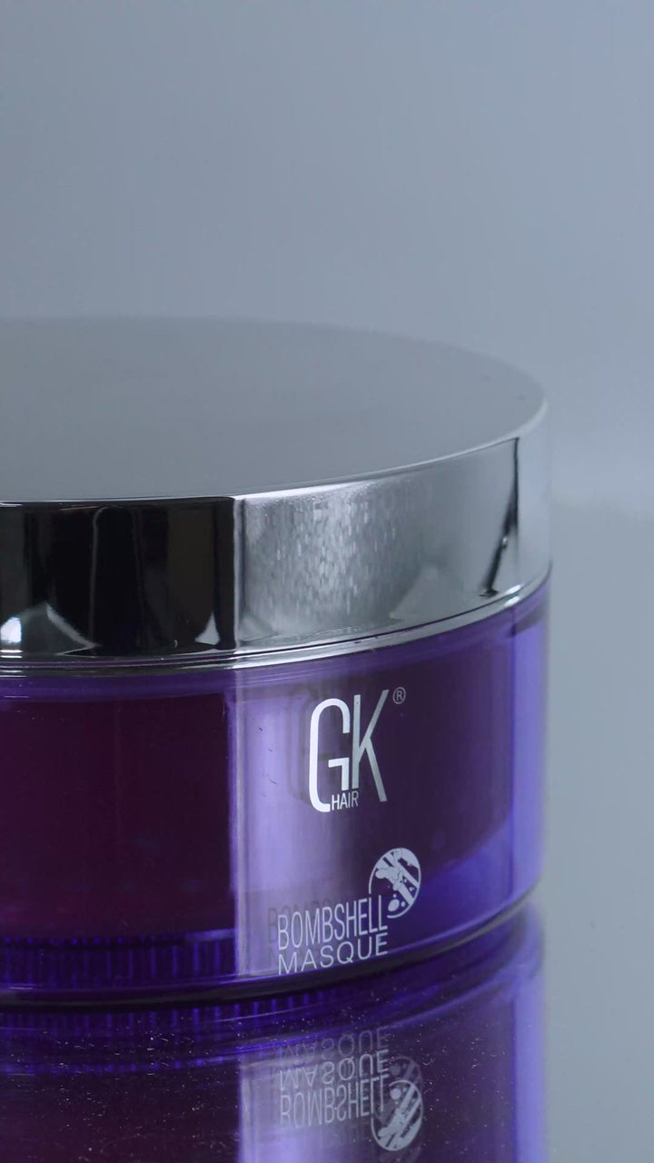 GK Hair Bombshell Masque purple jar with chrome lid, opened to show a deep red masque swirled and lifted on a spatula