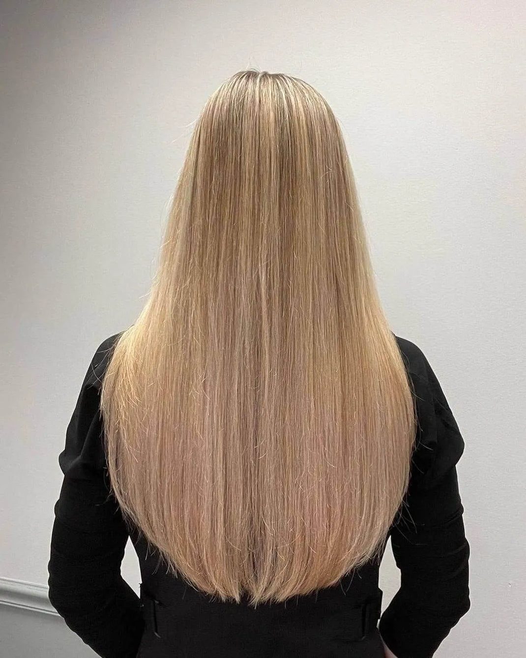 Woman seen from behind in a black long-sleeved top, her blonde hair falling sleek and shiny in a soft V-shaped hemline